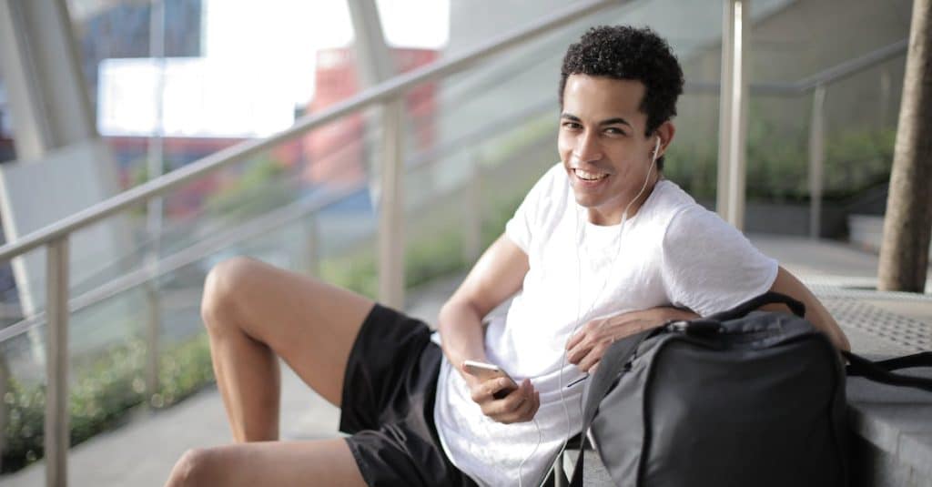 delighted-african-american-man-in-earphones-and-sportswear-smiling-at-camera-while-sitting-with-big