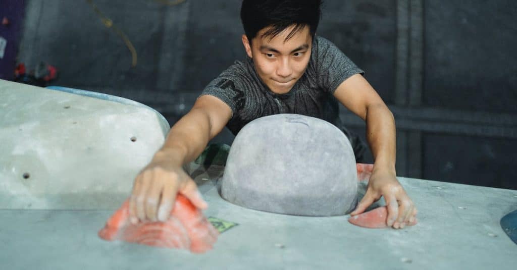 strong-asian-man-clambering-wall-in-gym